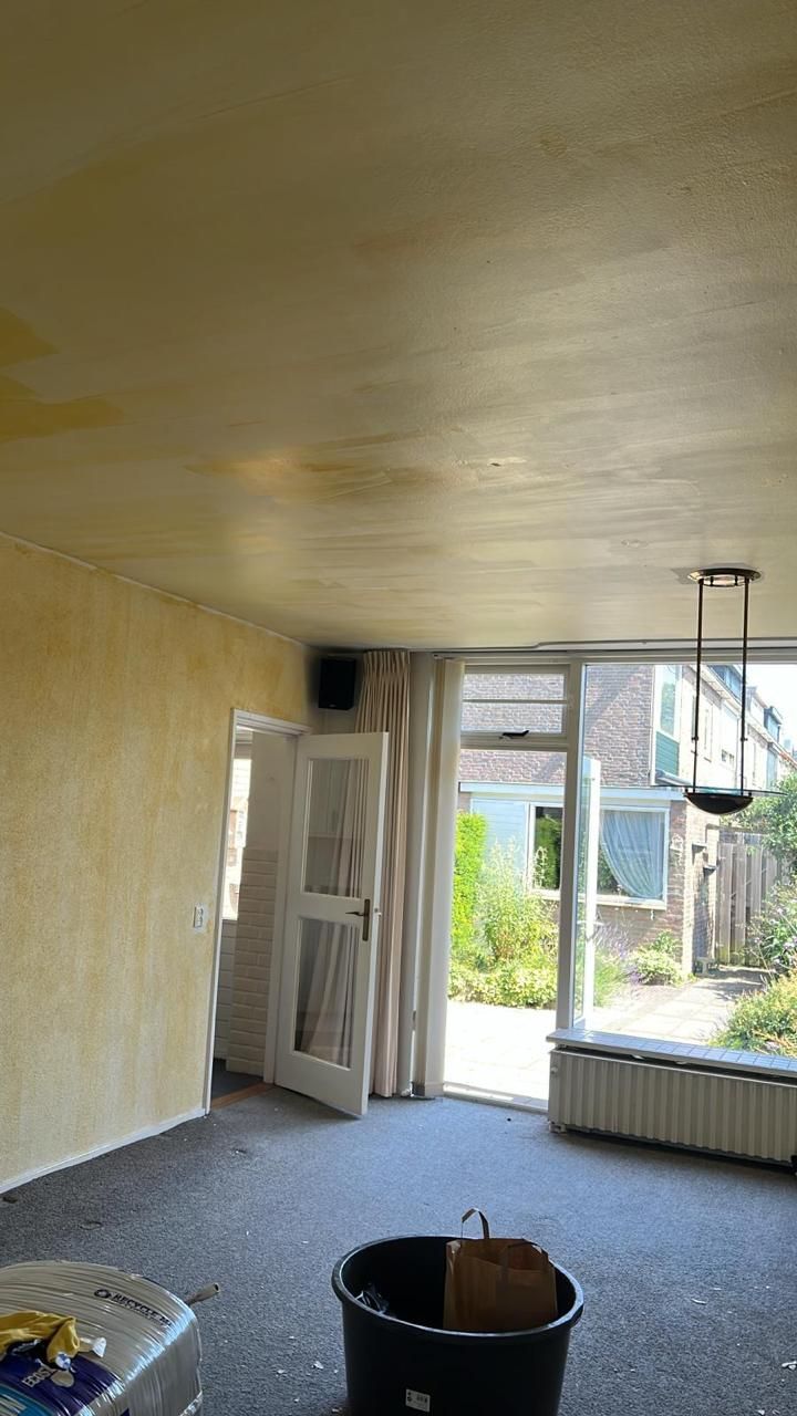 Woonkamer met gele lijmresten op plafond en wanden