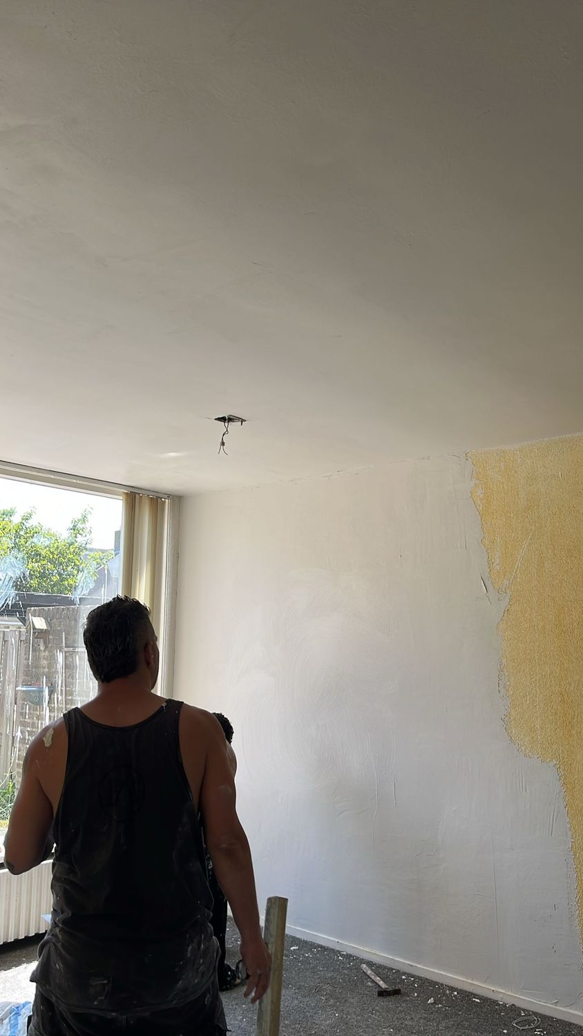 Stukadoor werkt aan een woonkamerwand, half wit en half nog geel