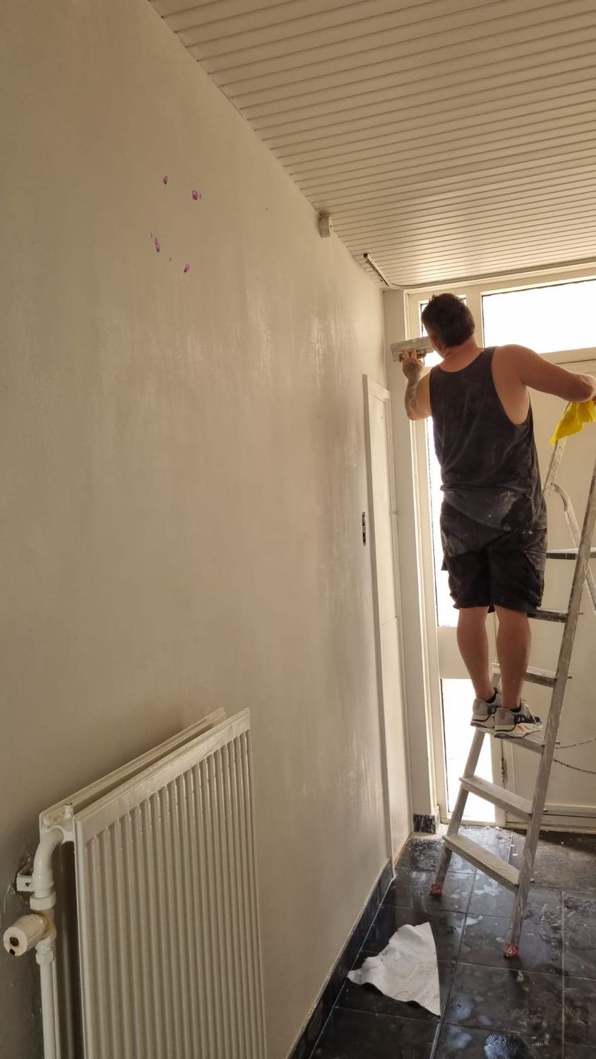 Stukadoor op een ladder werkt de halwand af bij de voordeur