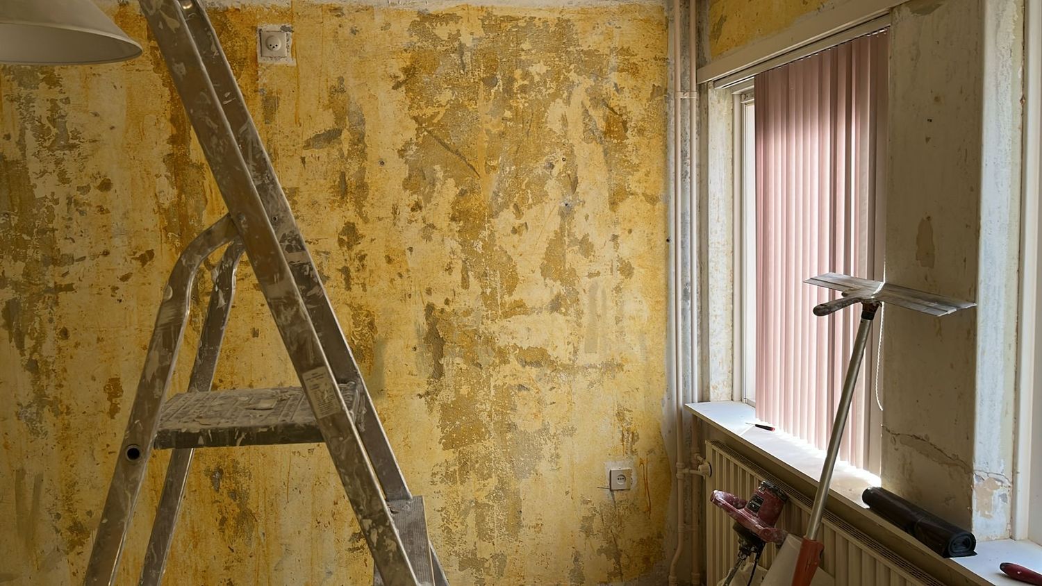 Halwand met lijmresten, raam met lamellen en radiator